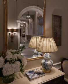 a lamp is sitting on a table next to a mirror and vase with flowers in it