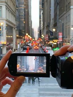 someone holding up a camera in the middle of a city street with buildings on both sides