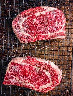 two raw steaks sitting on top of a grill