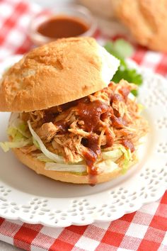 a pulled pork sandwich on a bun with lettuce and tomato sauce sitting on a white plate