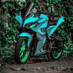 a blue and black motorcycle parked in front of some bushes with green leaves on it