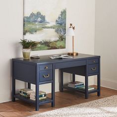 a painting hangs on the wall above a desk with books and a lamp next to it