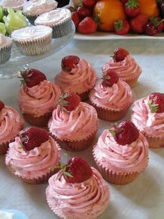 several cupcakes with pink frosting and strawberries on top next to some fruit