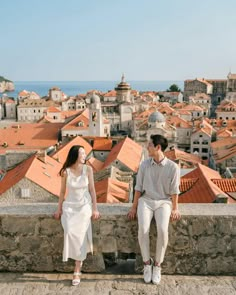 a man and woman sitting on top of a stone wall next to each other in front of a city