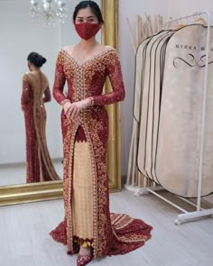 a woman in a red and gold dress standing next to a mirror with her face covered