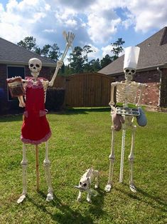 two skeleton statues standing in the grass with one holding a tray and another holding a dog