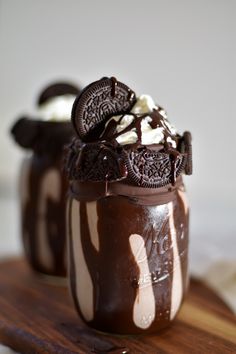 two jars filled with chocolate ice cream and oreo cookies on top of a wooden cutting board