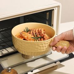 a person holding a bowl with food in it near an open microwave door on a counter