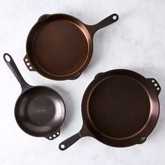 three frying pans sitting on top of a white counter next to each other