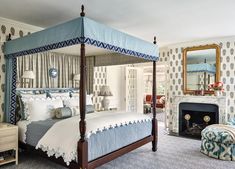 a bedroom with blue and white bedding, fireplace and mirror on the wall next to it