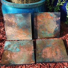 four square rusty tiles sitting on the ground next to a potted plant