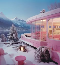 a pink bus is parked on the snow covered ground near some trees and mountains in the background