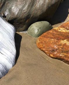 some rocks and sand on the beach with one rock sticking out of it's side