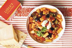 a white bowl filled with pasta and vegetables next to a red and white striped table cloth