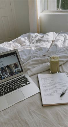 an open laptop computer sitting on top of a bed next to a cup of coffee