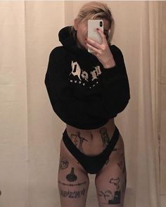 a woman with tattoos taking a selfie in front of a shower curtain while wearing a black hoodie