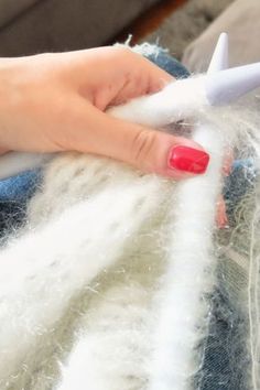 a woman is using a needle to cut through the yarn