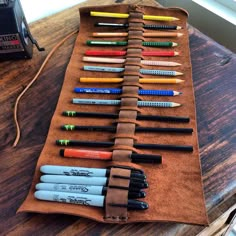 an assortment of pens and pencils are lined up on a piece of brown fabric