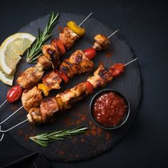 chicken skewers with marinara sauce and lemon wedges on a black plate