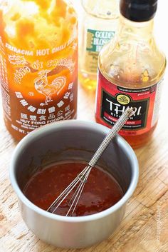 a bowl filled with sauce next to bottles of hot sauce and a whisk