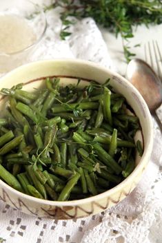 a white bowl filled with green beans on top of a lace table cloth next to silverware