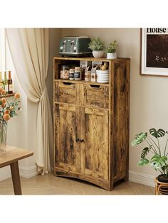 a wooden cabinet sitting in front of a window next to a potted plant on top of a table