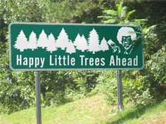 a sign that says happy little trees ahead on the side of a road in front of some trees