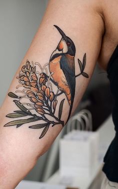 a bird sitting on top of a plant next to a person's arm with flowers