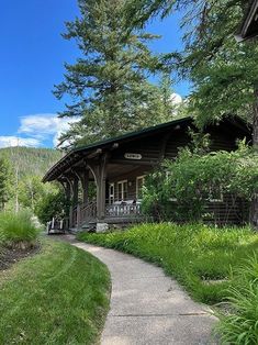 a small wooden cabin surrounded by lush green grass and trees, with a pathway leading to the front door