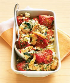 a casserole dish with tomatoes, cheese and herbs in it on a wooden table