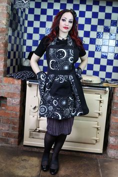 a woman standing in front of an oven wearing a black dress with white circles on it