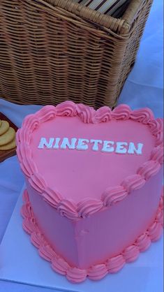 a pink heart shaped cake sitting on top of a table next to a basket filled with cookies