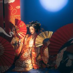 a geisha woman in traditional japanese dress holding two red and gold fan's