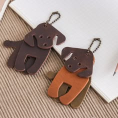 two leather dog key chains sitting on top of a notebook