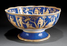 a blue and gold bowl with figures on it's sides, sitting on a black surface