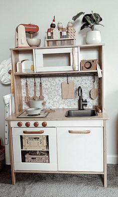 a wooden toy kitchen with white cabinets and drawers