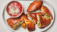 a white plate topped with pastries next to a bowl of tomato sauce and cheese