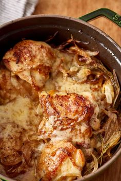 a pot filled with chicken and cheese on top of a wooden table next to a fork