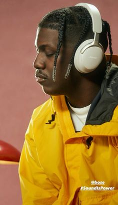 a man with headphones on sitting in front of a red wall wearing a yellow jacket