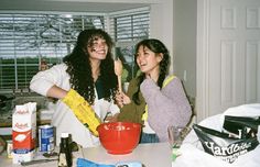 two young women standing in a kitchen with food on the counter and one holding a spatula