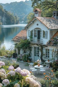 a white house sitting next to a body of water with flowers growing on it's side