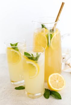 two glasses filled with lemonade and mint garnish next to some sliced lemons