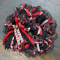 a red and black mesh wreath on the ground with ribbon around it, sitting on top of a wooden floor