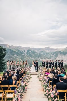 an outdoor ceremony with mountains in the background and people standing at the end of the aisle