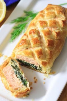 a pastry with salmon and spinach on it sits on a plate next to a lemon wedge