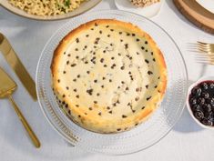 a table topped with a pie covered in cheese and black olives next to silverware