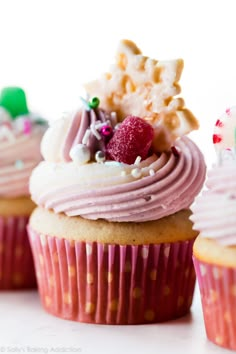 three cupcakes with pink frosting and sprinkles on top, one has a candle