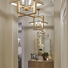 a hallway with a mirror, dresser and chandelier hanging from it's ceiling