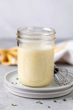 a glass jar filled with dressing sitting on top of a plate next to a whisk