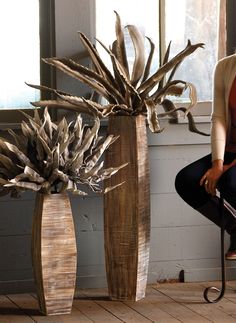 a woman sitting on a chair next to two tall vases with plants in them